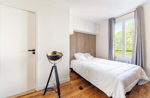 A bedroom with a bed, a standing lamp, a window with curtains, and a door. - Parisian Flat for Work and Study (Paris)