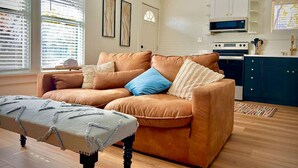 A modern living room with a brown leather sofa, a wooden bench, and a kitchen area with dark cabinets and a microwave.