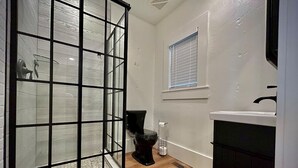A bathroom with a glass shower enclosure, a toilet, and a sink.