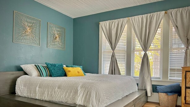 A bedroom with a large bed, a wooden bench, a wicker basket, and a wooden cabinet.