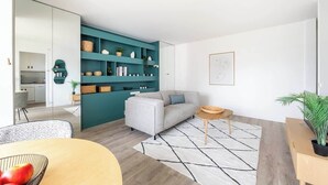 Uma sala de estar moderna com um sofá, uma mesa de centro, uma estante azul-turquesa e um espaço de jantar com mesa e cadeiras.