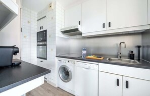 Une cuisine compacte équipée d’un lave-linge, d’une machine à café et d’un évier.