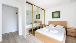 Um quarto com uma cama grande, uma mesa de cabeceira, um guarda-roupa com espelho e um quadro na parede.