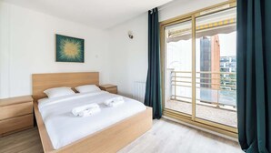 Quarto de hotel com uma cama grande, mesa de cabeceira, luminária na parede e uma janela com cortinas.