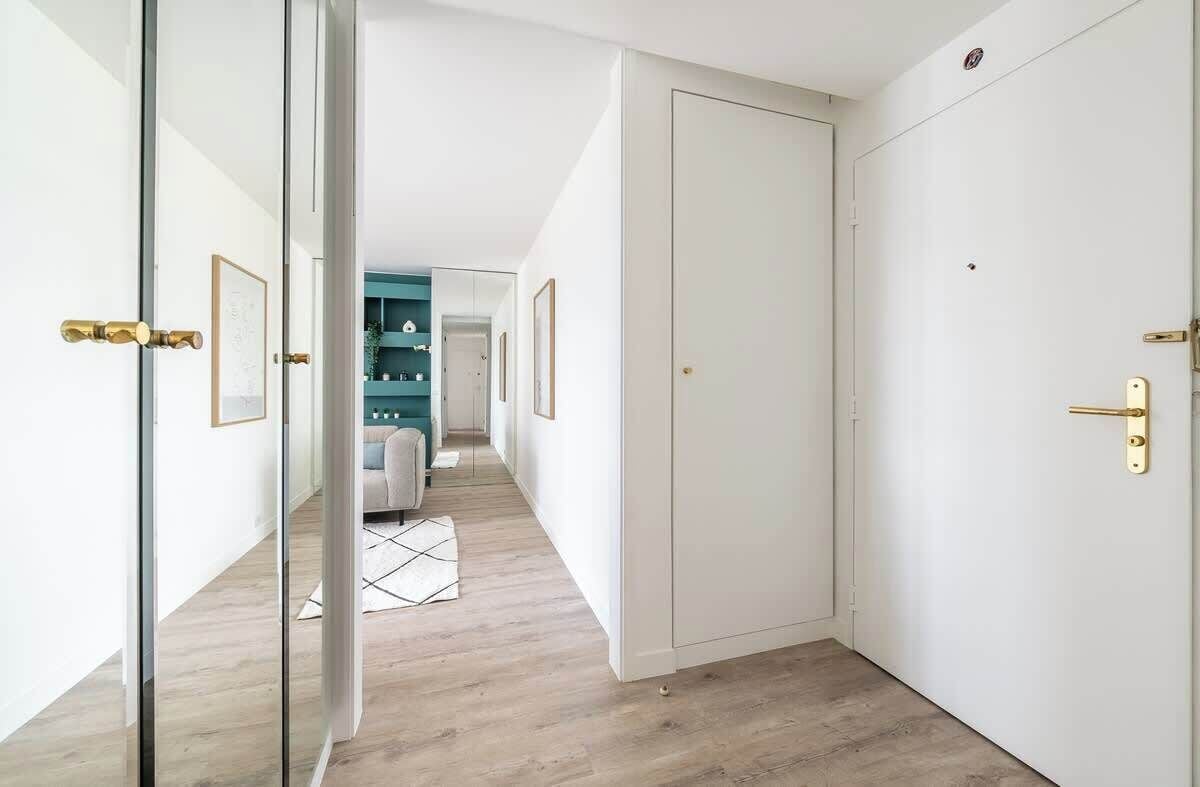 A hallway with a wooden floor, white walls, and a door with a gold handle.