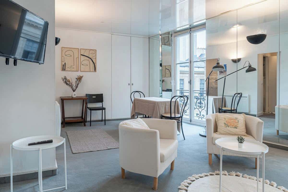 A modern living room with a sofa, armchairs, a small table, and a TV mounted on the wall.