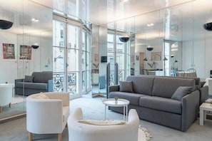 Un salón moderno con un sofá gris, sillones blancos y una mesita redonda.