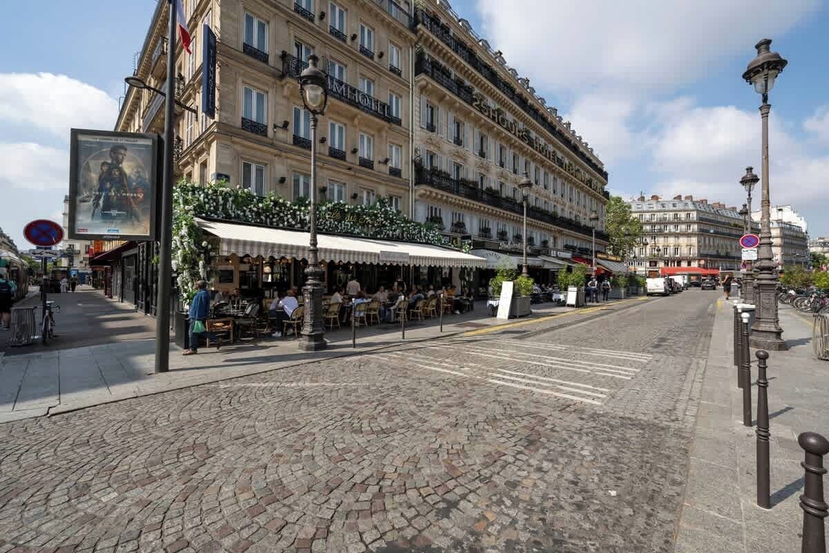 A cobblestone street with outdoor seating, a building with 'HOTEL' signage, and a clear blue sky.