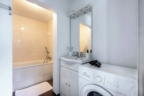 A modern bathroom with a bathtub, a sink, a mirror, and a washing machine.