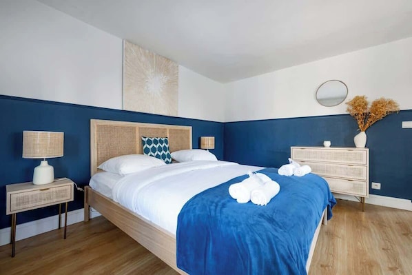 A bedroom with a bed, bedside tables, a dresser, a mirror, and a wall art piece.