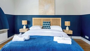 Camera d'albergo con un letto grande, due comodini con lampade, un elemento decorativo a parete e asciugamani piegati con cura.