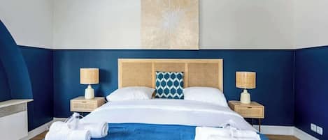 A hotel room with a large bed, two bedside tables with lamps, a decorative wall piece, and neatly folded towels.