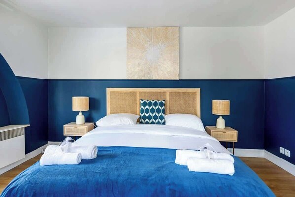 Habitación de hotel con una cama grande, dos mesitas de noche con lámparas, un adorno en la pared y toallas dobladas con cuidado.