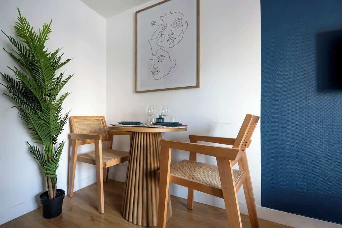 Ein Essbereich mit einem runden Holztisch, zwei Stühlen, einer Topfpflanze und einem gerahmten Kunstwerk an der Wand.