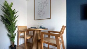 Zona pranzo con tavolo rotondo in legno, due sedie, una pianta in vaso e un quadro appeso al muro.