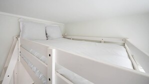 Una cama litera blanca con dos almohadas, cabecera blanca y colchón blanco.