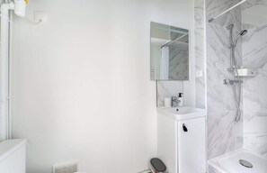 Un bany modern amb un lavabo blanc, un mirall i una dutxa amb un mur de marbre.