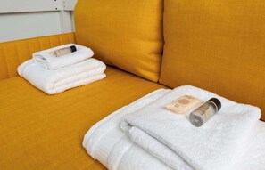 A room with a yellow sofa, two white towels, and two bottles of lotion.