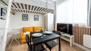 Una habitación con una mesa de comedor preparada para dos personas, un sofá con cojines amarillos, un televisor y un techo de listones de madera.
