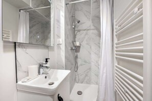 Baño con lavamanos blanco, espejo y ducha.