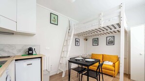 Una habitación compacta con una cama litera, una kitchenette pequeña, una mesa de comedor con sillas y un sofá.