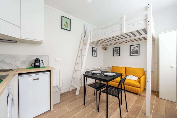 A compact room with a bunk bed, a small kitchenette, a dining table with chairs, and a sofa.