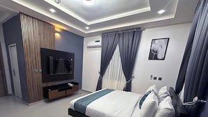 A modern bedroom with a bed, TV, and built-in storage unit. - 99 Mozilla Apartments (Abuja)