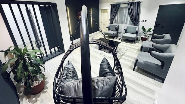 A modern living room with a hanging chair, grey sofas, and a potted plant. - 99 Mozilla Apartments (Abuja)