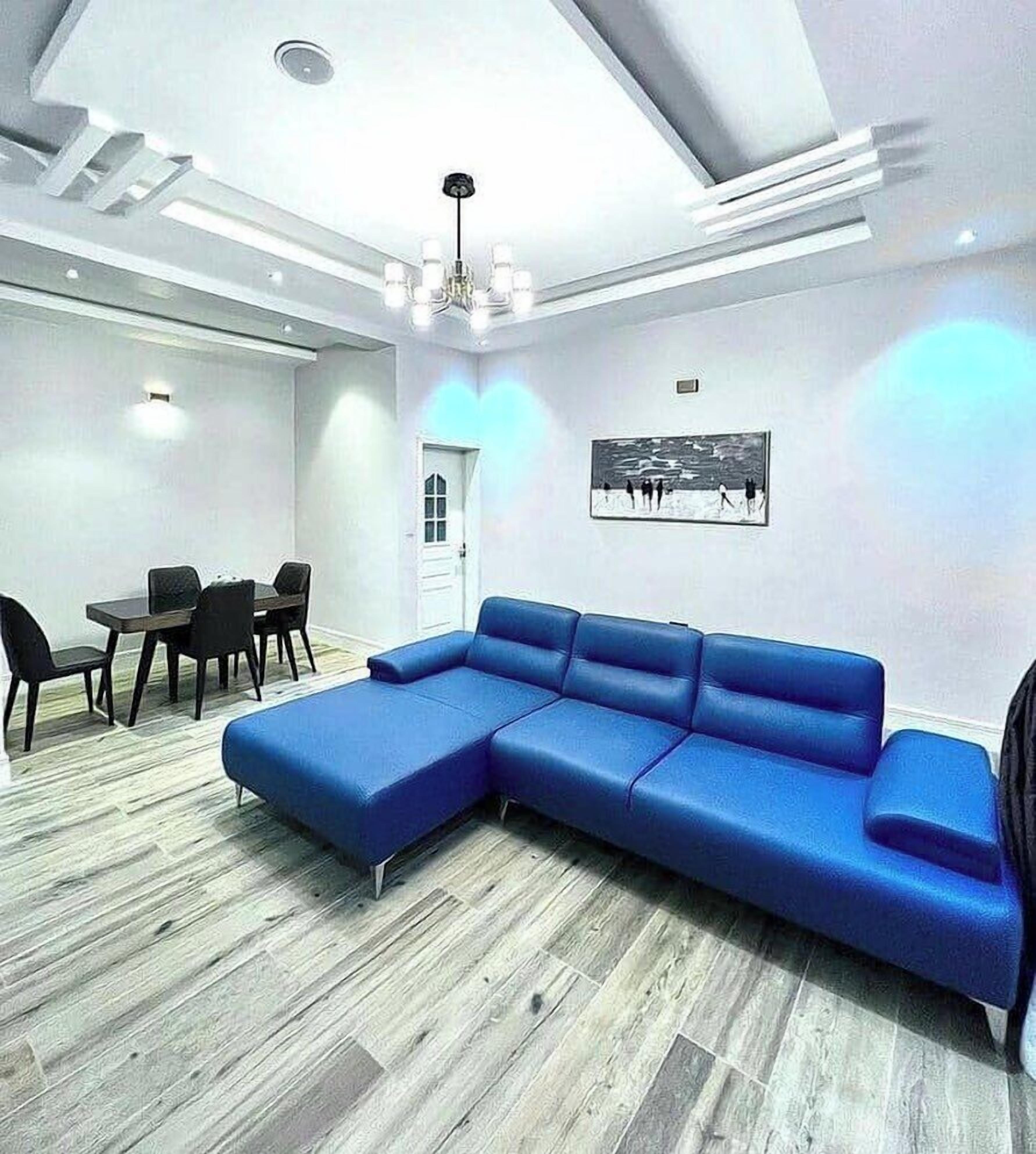 Un salon moderne avec un canapé d’angle, un coin repas comprenant des chaises et une table, et un tableau accroché au mur.