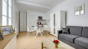 A modern living room with a grey sofa, a wooden coffee table, and a dining area with white chairs.