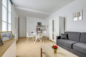 A modern living room with a grey sofa, a wooden coffee table, and a dining area with white chairs.