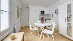 A compact kitchen with white cabinets, a microwave, and a dining area with a white table and chairs.