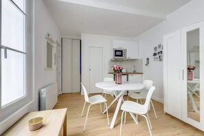 A compact kitchen with white cabinets, a microwave, and a dining area with a white table and chairs. - Center of Paris : Fully equipped and Cozy (Paris)