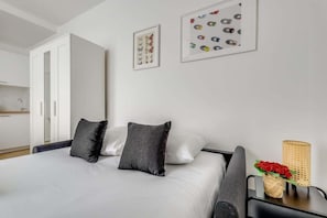 A neatly arranged bedroom with a bed, pillows, a nightstand, a lamp, and two framed pictures on the wall.