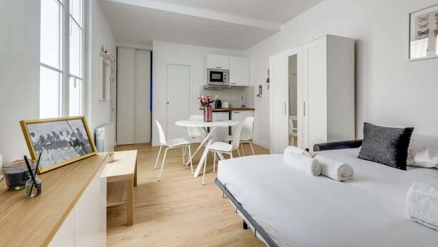 A modern hotel room with a bed, a desk, and a kitchenette.