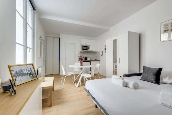 A modern hotel room with a bed, a desk, and a kitchenette.