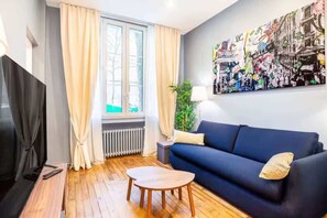 Una sala de estar con un sofá azul oscuro, una mesa de centro de madera, un televisor y una ventana con cortinas.
