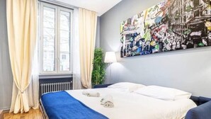 Et hotelværelse med en seng, et vindue med gardiner, en radiator og et billed på væggen.