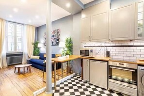 A compact kitchen with a microwave, oven, and refrigerator. There is a dining area with a table and chairs, and a sofa in the adjacent living room.