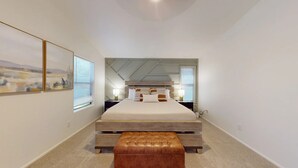 A modern bedroom with a large bed, a wooden bench, and a mirror above the bed.