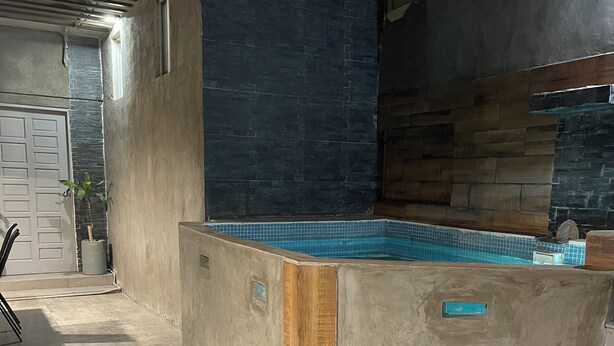 A pool area with a stone wall, wooden furniture, and a tiled floor. - House with Jacuzzi (La Paz)