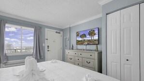 A hotel room with a large bed, a television mounted on the wall, a dresser, and a door. - Bluewater Resort 1106 (Myrtle Beach)