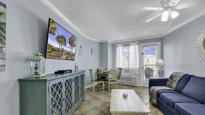 A living room with a TV, a dining table with chairs, a blue sofa, and a ceiling fan. - Bluewater Resort 1106 (Myrtle Beach)