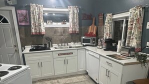 Une cuisine avec des meubles blancs, une cuisinière, un four à micro-ondes et un évier.