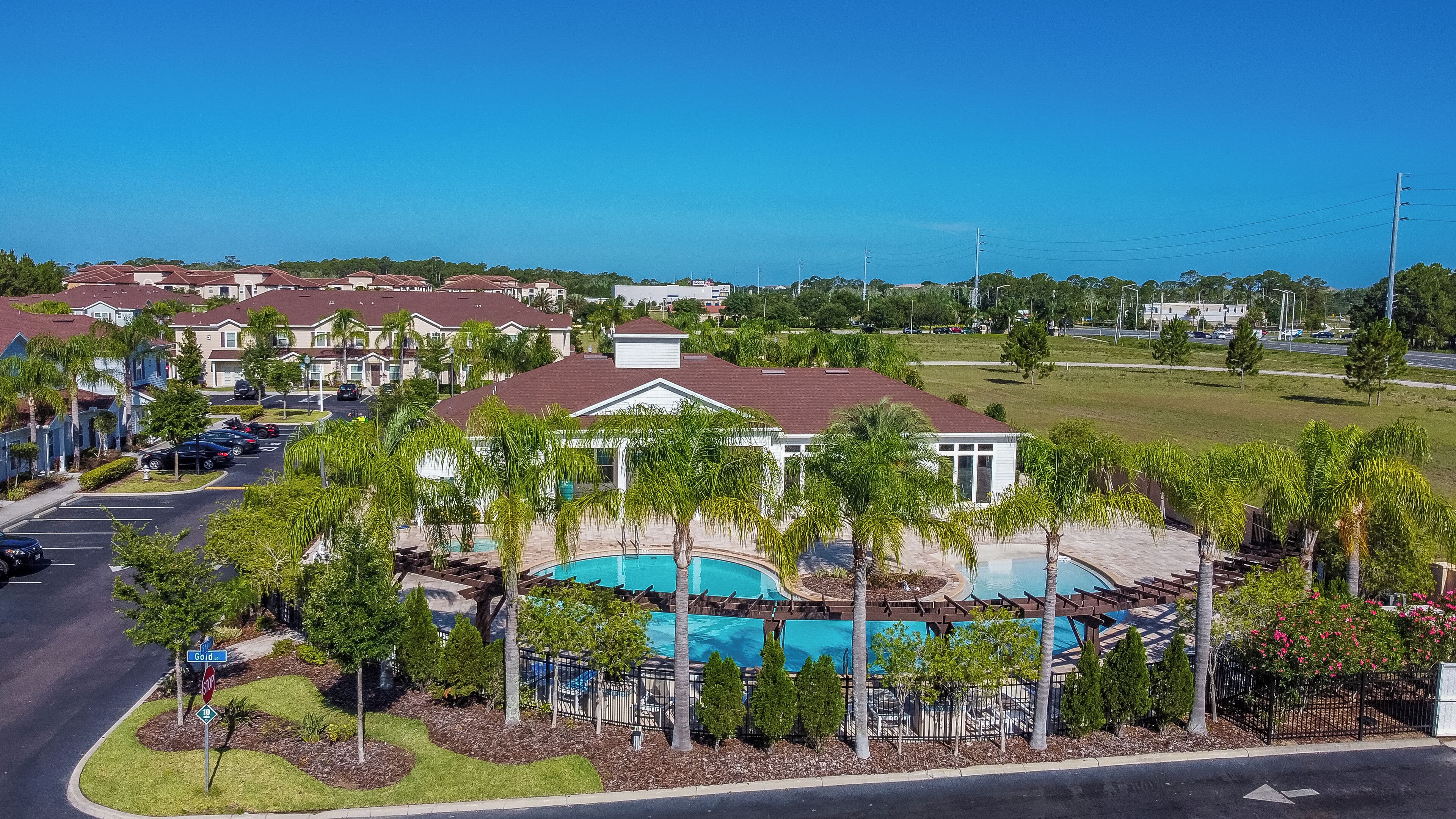 A residential area with a large house featuring a swimming pool, surrounded by palm trees and a clear view of the ocean.