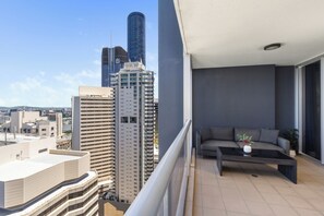 Un balcon avec un canapé et une table basse, donnant sur un paysage urbain avec de hauts immeubles.