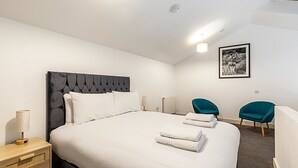 A modern hotel room with a large bed, two chairs, a bedside table with a lamp, and a framed picture on the wall. - Stylish Camden Flat Near Markets & Tube (London)