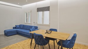 Ein modernes Wohnzimmer mit einem blauen Ecksofa, einem Holzessttisch mit vier Stühlen und einem Fischgrätparkettboden.