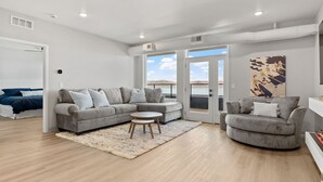 Una sala moderna con un sofá seccional gris, una mesa de centro redonda y vistas al exterior.