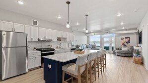 Una cocina moderna con armarios blancos, un refrigerador de acero inoxidable y una isla central con taburetes de bar.